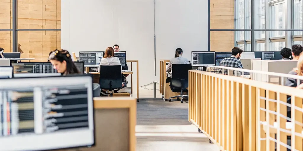 Software developers working at multiple computer stations inside a modern open-plan office.